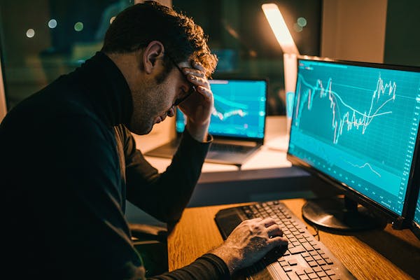 man sits exhausted at his home office, staring at his computer screen filled with financial data