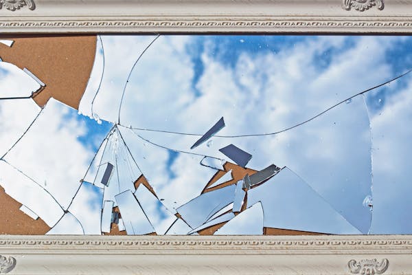 Dusty broken mirror in a vintage white frame, the reflection of blue sky and clouds