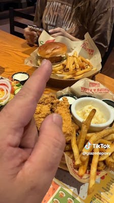 hand pointing at a sandwich and fries
