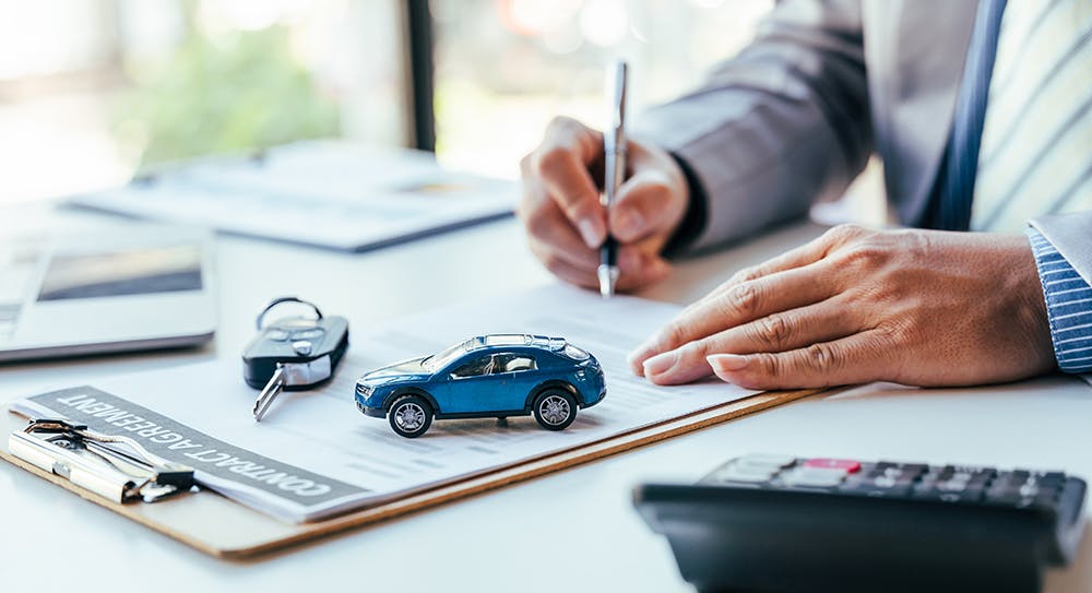 Man signing car insurance document or lease paper. Writing signature on contract or agreement. Buying or selling new or used vehicle. Car keys on table. Warranty or guarantee. Customer or salesman.