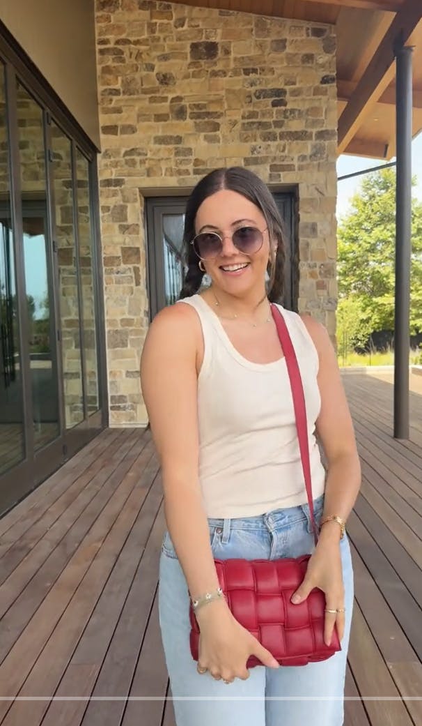 Boots and a slick back bun video with a woman in a white tank top with a red bag.