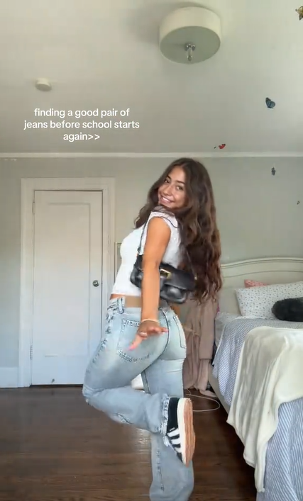 A young brunette woman showing off her outfit. Text overlay reads, "finding a good pair of jeans before school starts again >>"