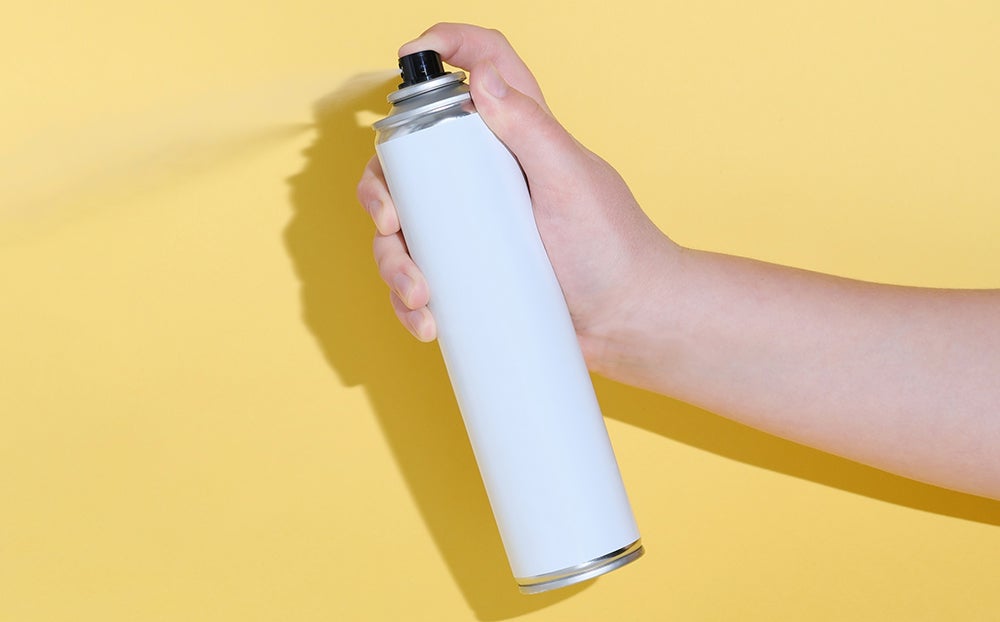 hand holding a tin can and spraying a product over a yellow background. mock up for product design. hygiene or insecticide. cleaning and householding chemistry.