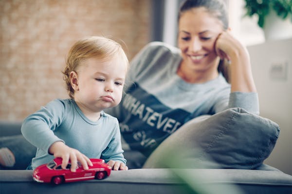 Mom and her toddler son plays with red car in their cosy living room