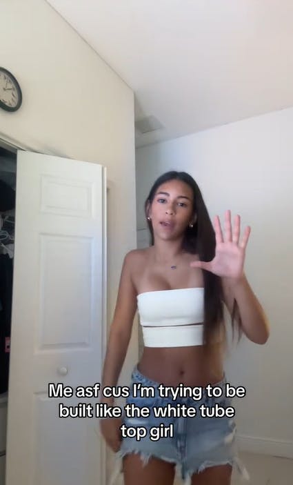 Screenshot of a woman in a white tube top and jean shorts. Text overlay reads, 'Me asf cus I'm trying to be built like the white tube top girl.'