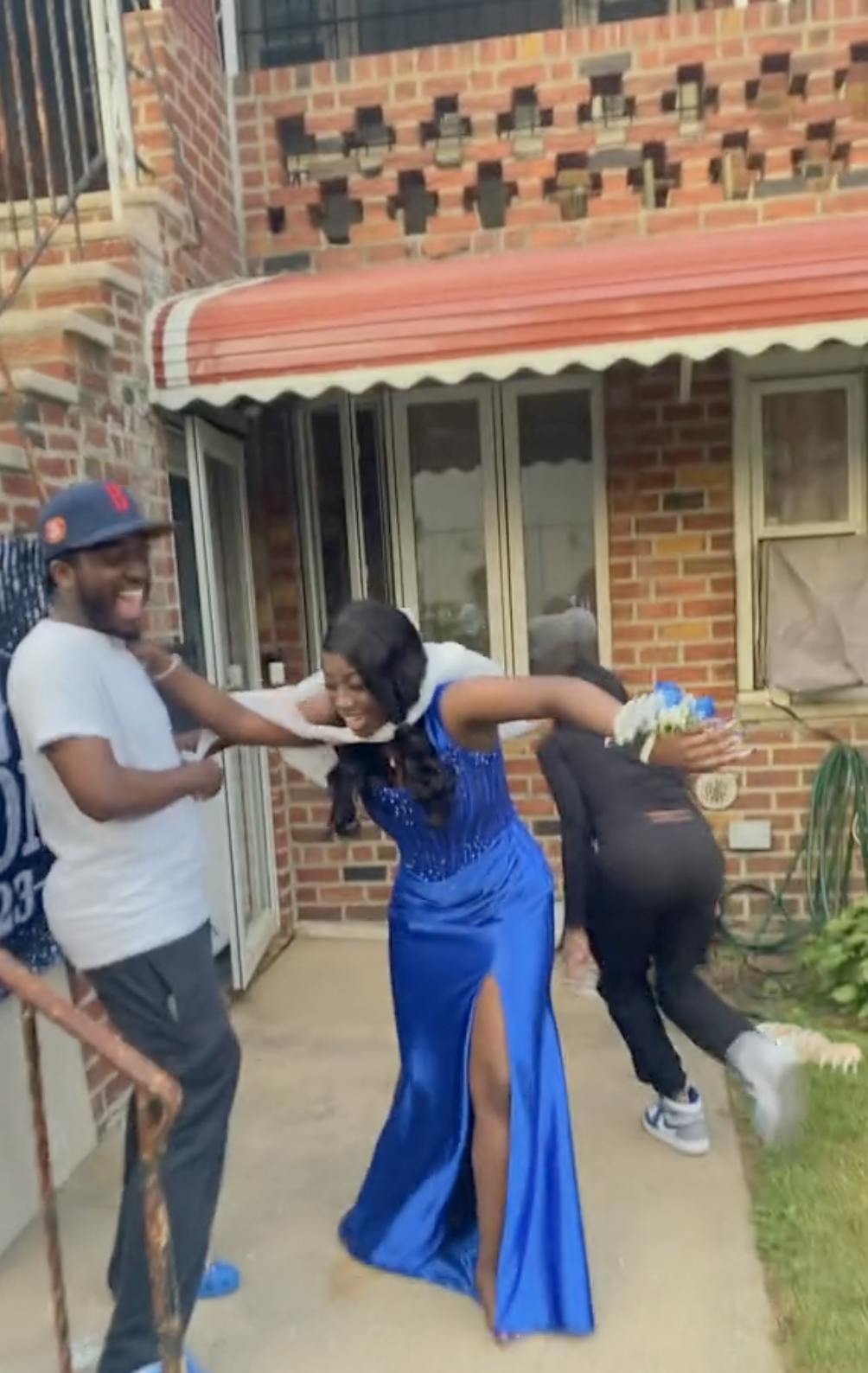 Woman in a ballgown with two people on either side trying to tear a plastic bag around her and failing, almost choking her.