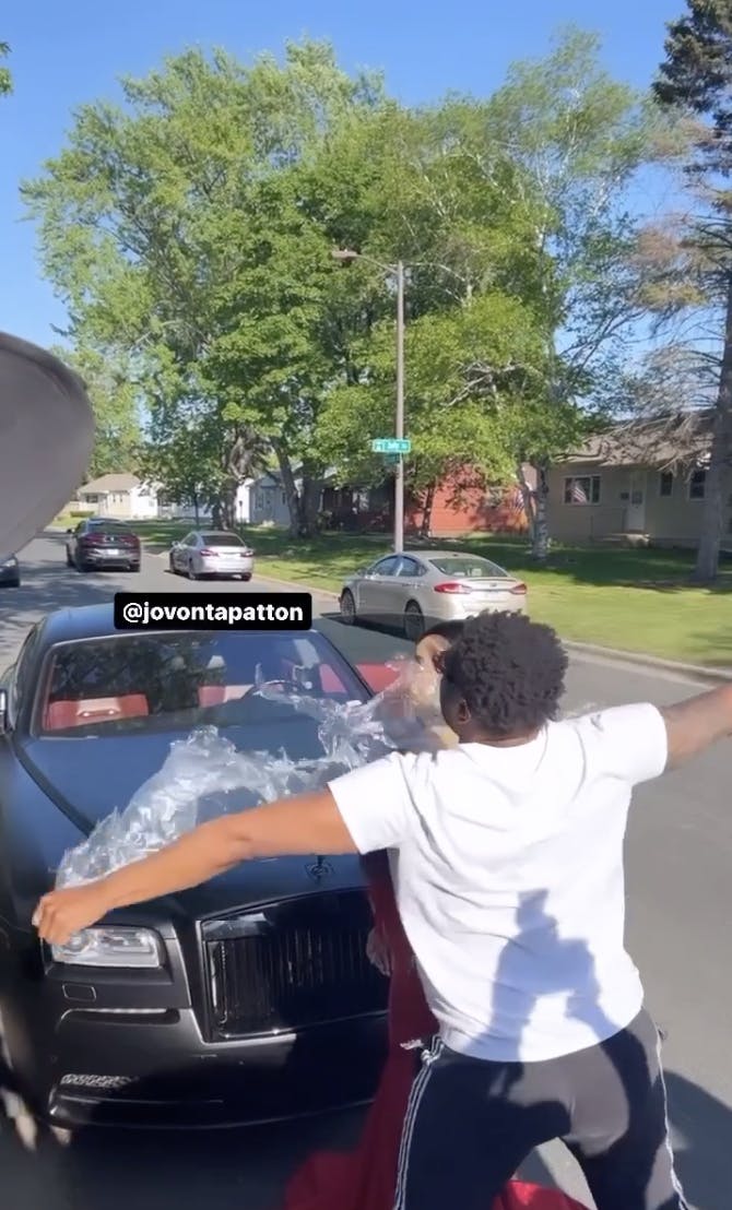 A man tearing apart a plastic bag that was covering a young woman in a prom dress.