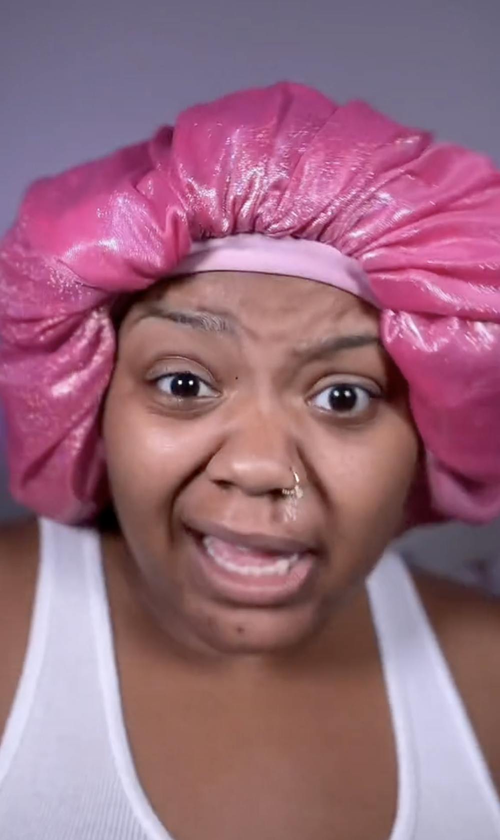 Woman in a pink bonnet looking concerned at the camera.