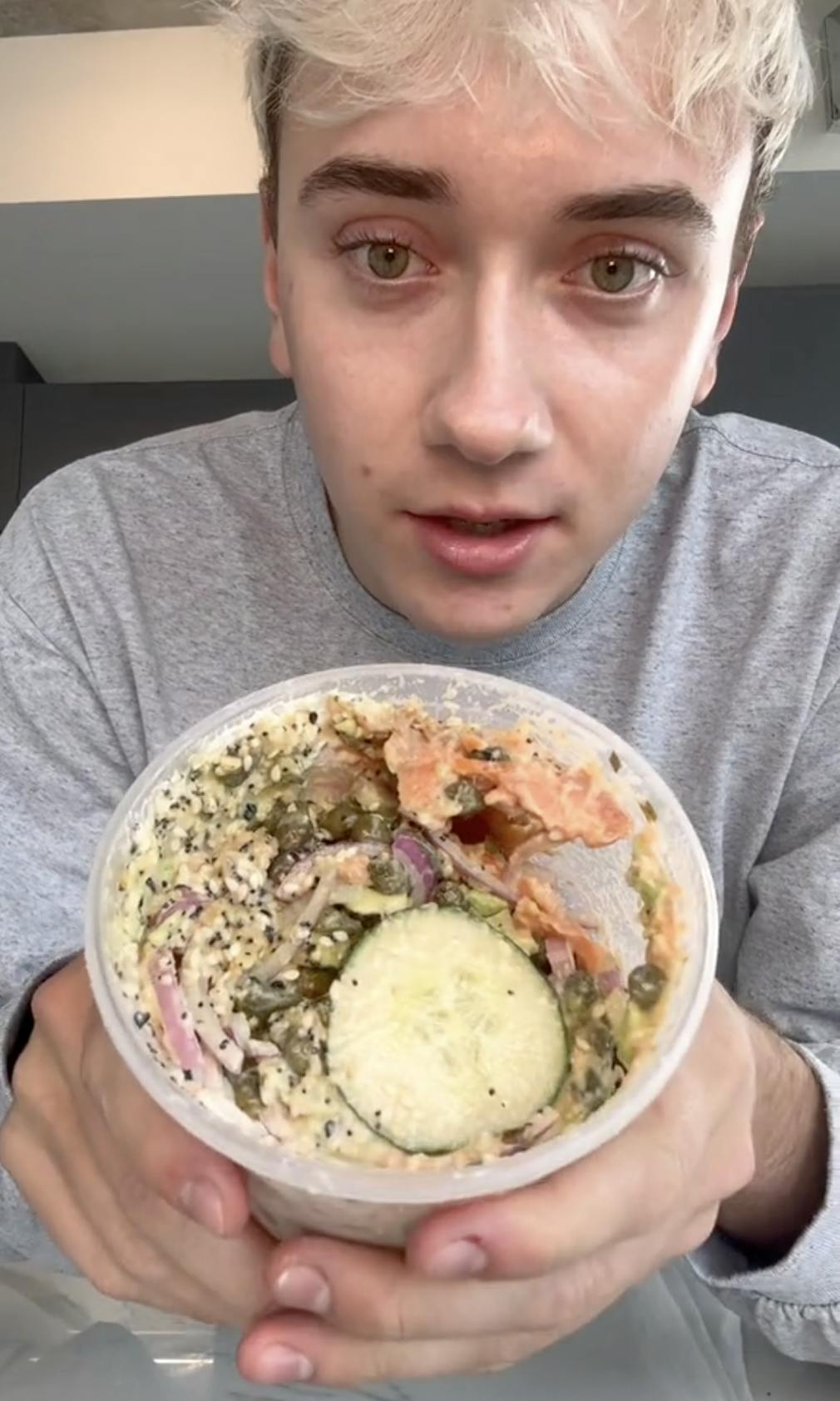 A young man with blond hair showing off the cucumber salad he made for the camera.