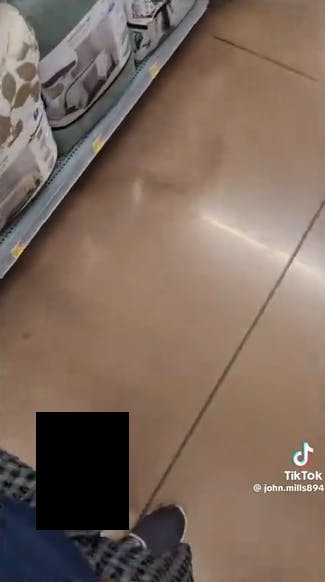 Screenshot from a TikTok video pointed downward in a Walmart store, a black box covering the front of the man's pants where he has revealed himself.