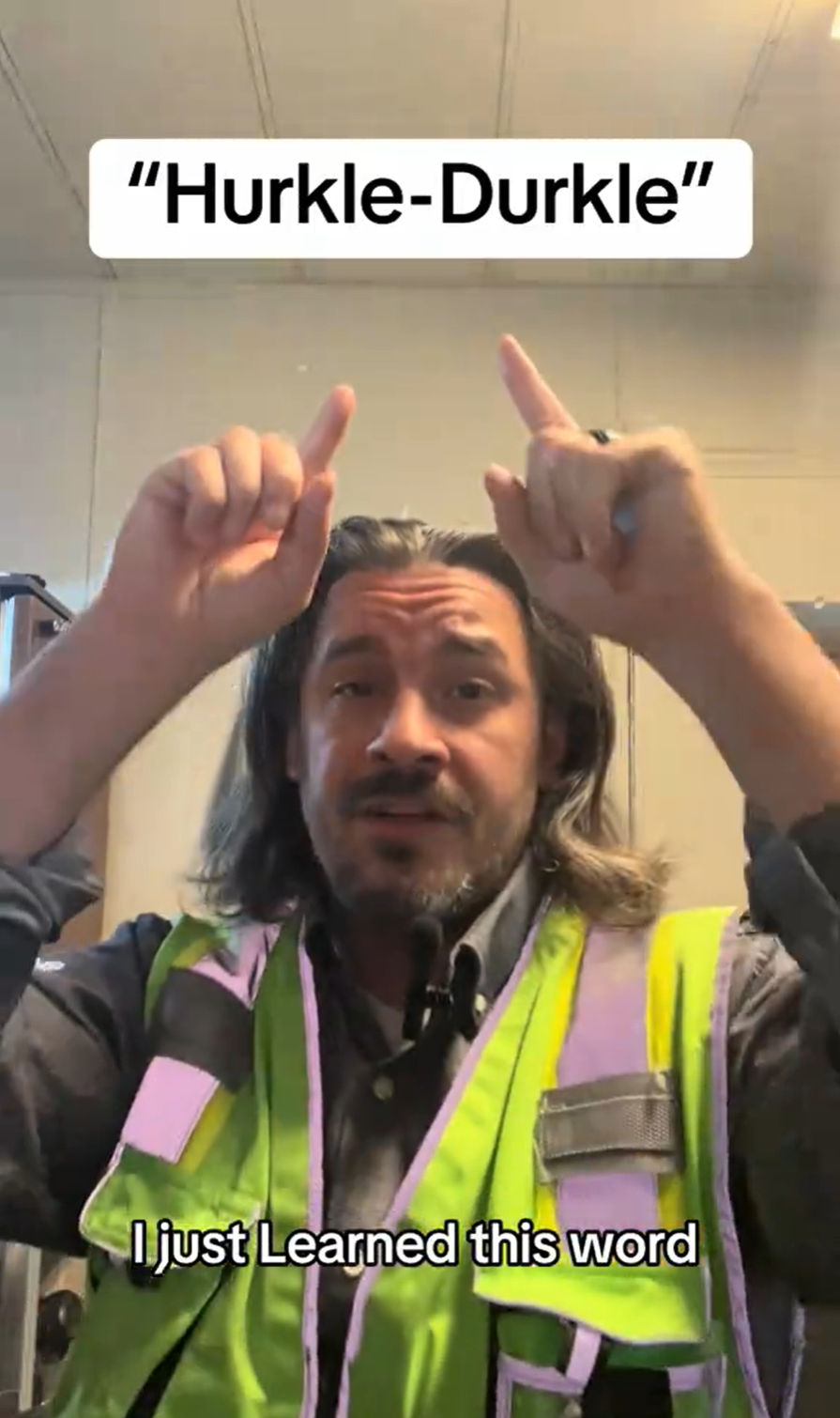 A man with long hair in a hi-viz vest pointing at the words'hurkle-durkle' on the screen.