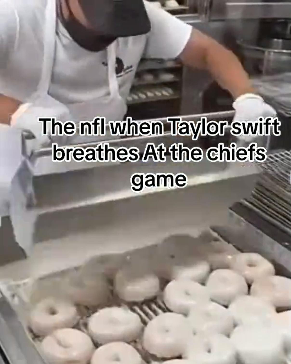 A baker putting icing on over a dozen donuts at the same time. Text overlay reads, 'The nfl when Taylor swift breathes At the chiefs game.'