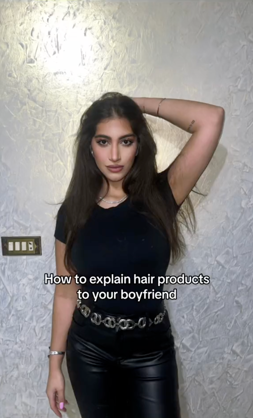 Screenshot of a woman's TikTok of her posing against a white wall. Text overlay reads, 'How to explain hair products to your boyfriend.'