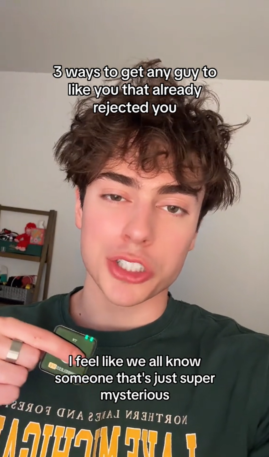 A man with messy hair is talking into the camera while holding a lapel mic in his hand. Text overlay reads, '3 ways to get any guy to like you that already rejected you.' A second text box reads, 'I feel like we all know someone that's just super mysterious.'