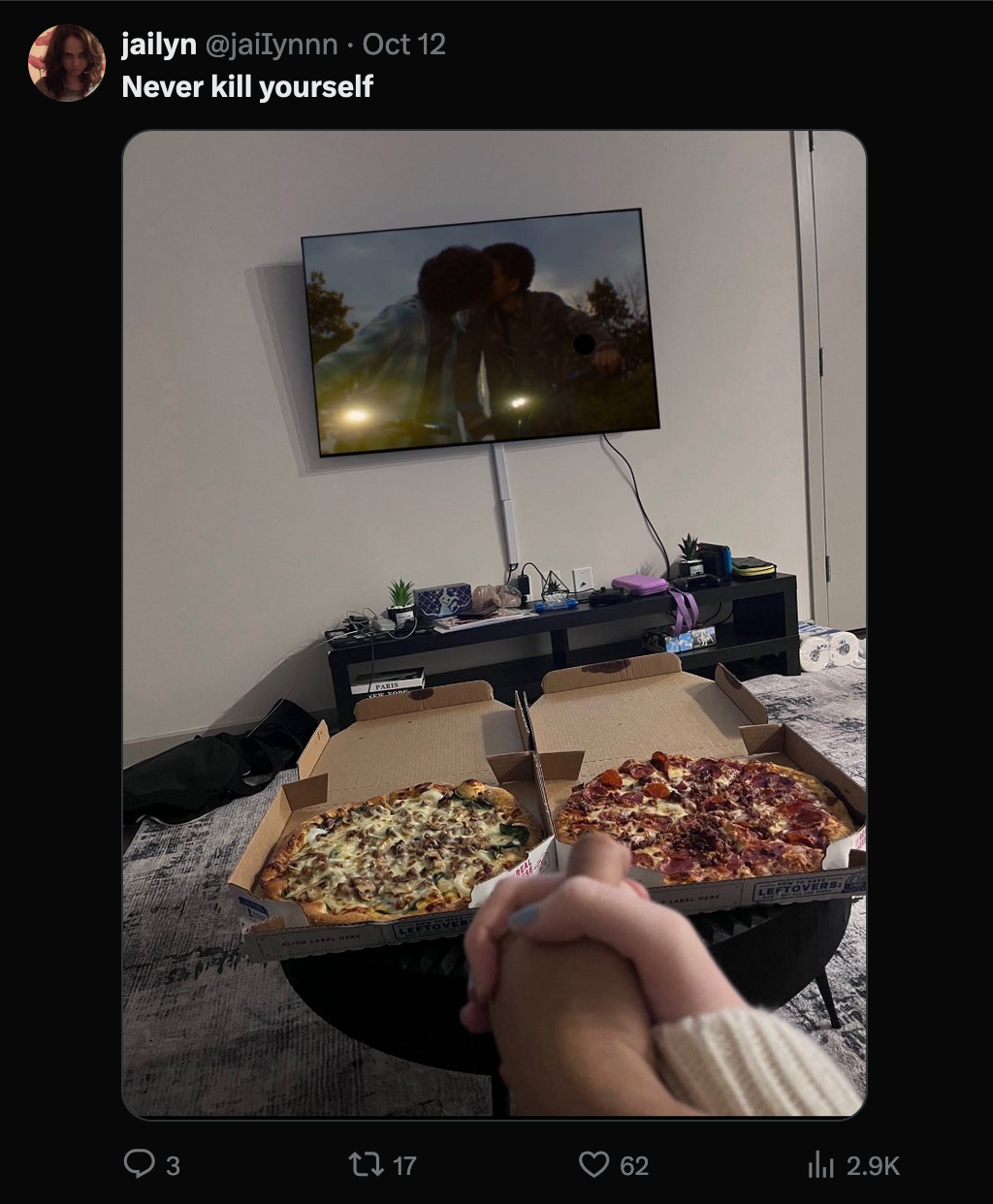 X post of a photo of two hands clasped over two personal pizzas, while a monitor above the pizzas showinf the home screen of the fantasy game 'Elden Ring.' The caption of the X post is 'never kill yourself.'