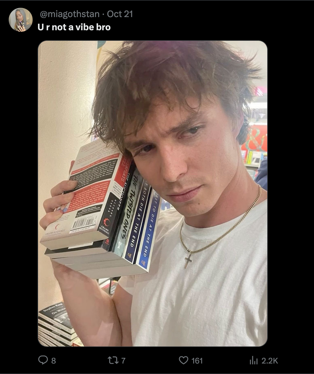 An X post of a young man with messy hair, holding a bunch of books up to his face knowingly. The caption reads 'U R Not a Vibe Bro'