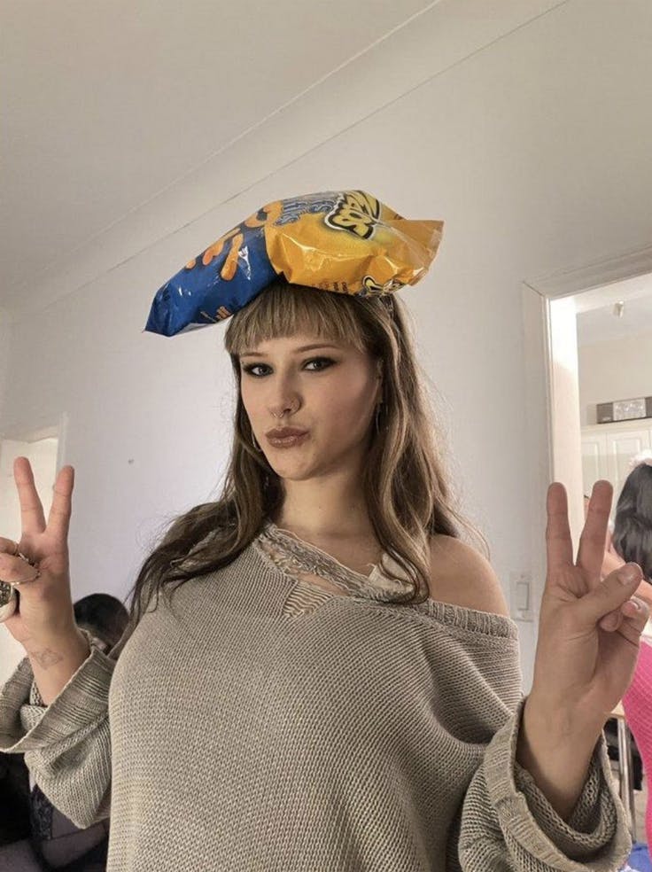 Woman in a sweater with a bag of chips on her head, and peace signs