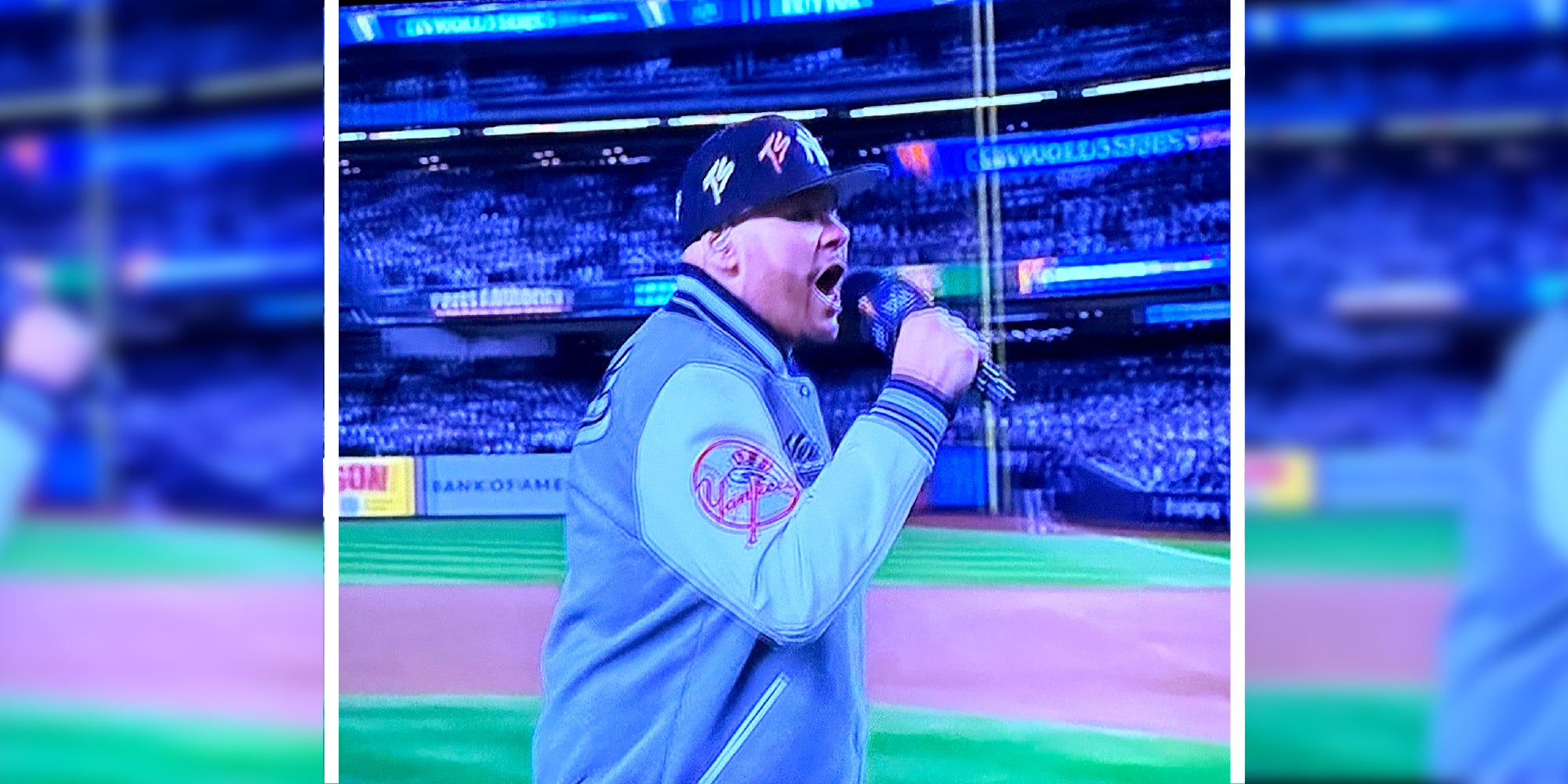 A photo from a screen of the rapper Fat Joe speaking into a microphone in front of a baseball stadium crowd.