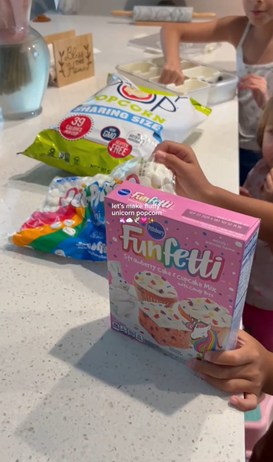 A family putting out ingredients for fluffy popcorn on their counter, including raw Funfetti flour.