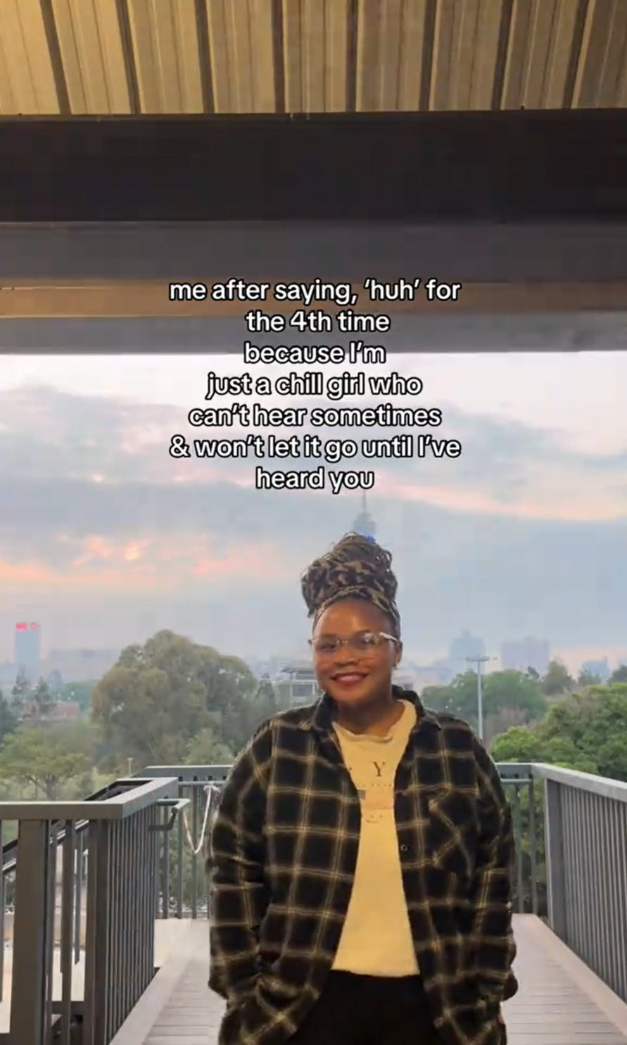 Woman standing on a balcony with her hands in her pockets. Text overlay reads, 'me after saying, 'huh' for the 4th time because I'm just a chill girl who can't hear sometimes & won't let it go until I've heard you.'