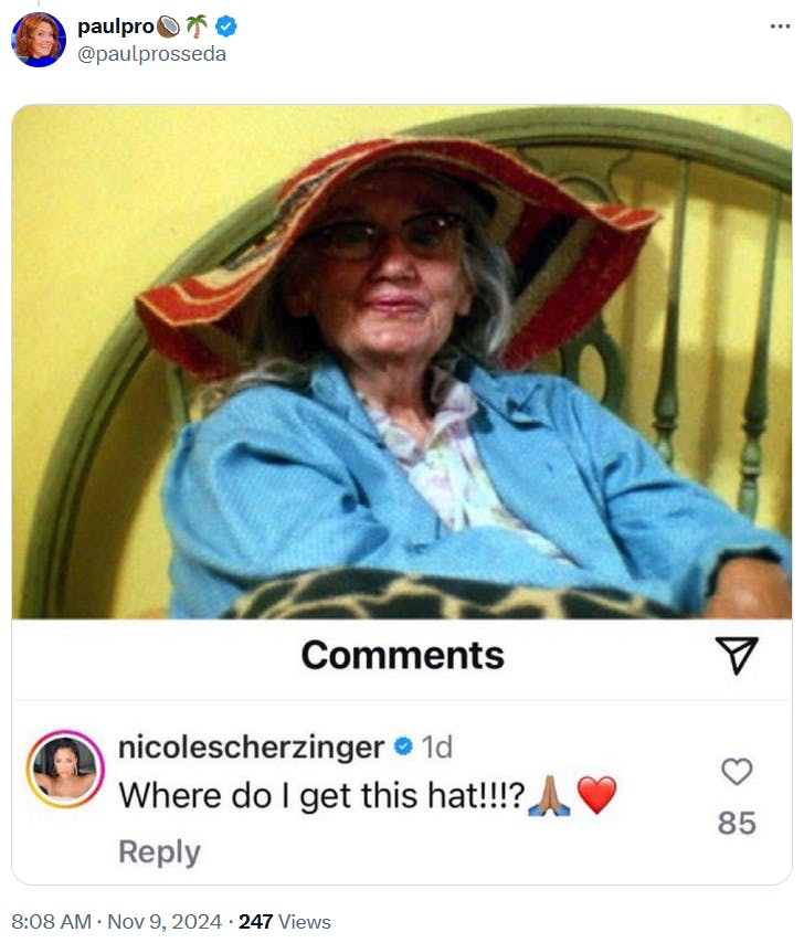 An elderly woman in a colorful sun hat sitting in a chair with a comment on her headwear.