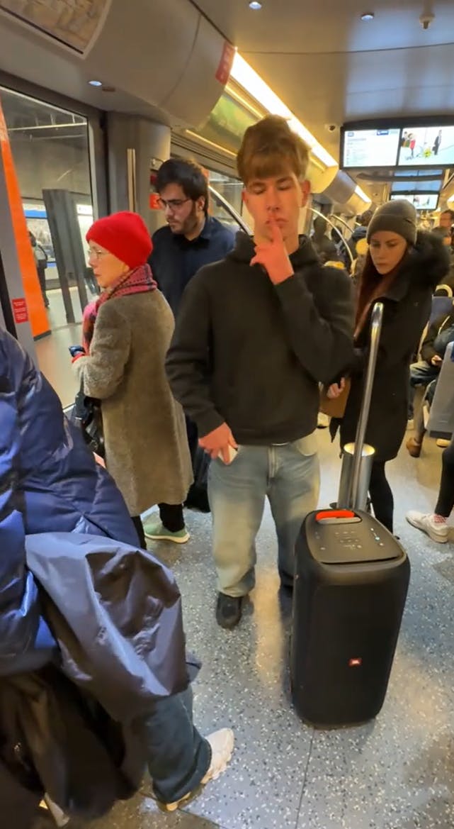 Original Sigma Sigma Boy of a man on a train touching his lips with a finger as he turns up the music.