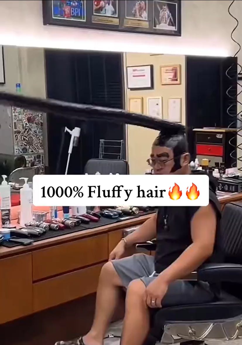 Sigma Sigma Boy trend with text overlay that reads, '1000% Fluffy hair (fire emojis)' with a man sitting in a barber's chair with what looks like black taped hair jutting out four feet in front of him.