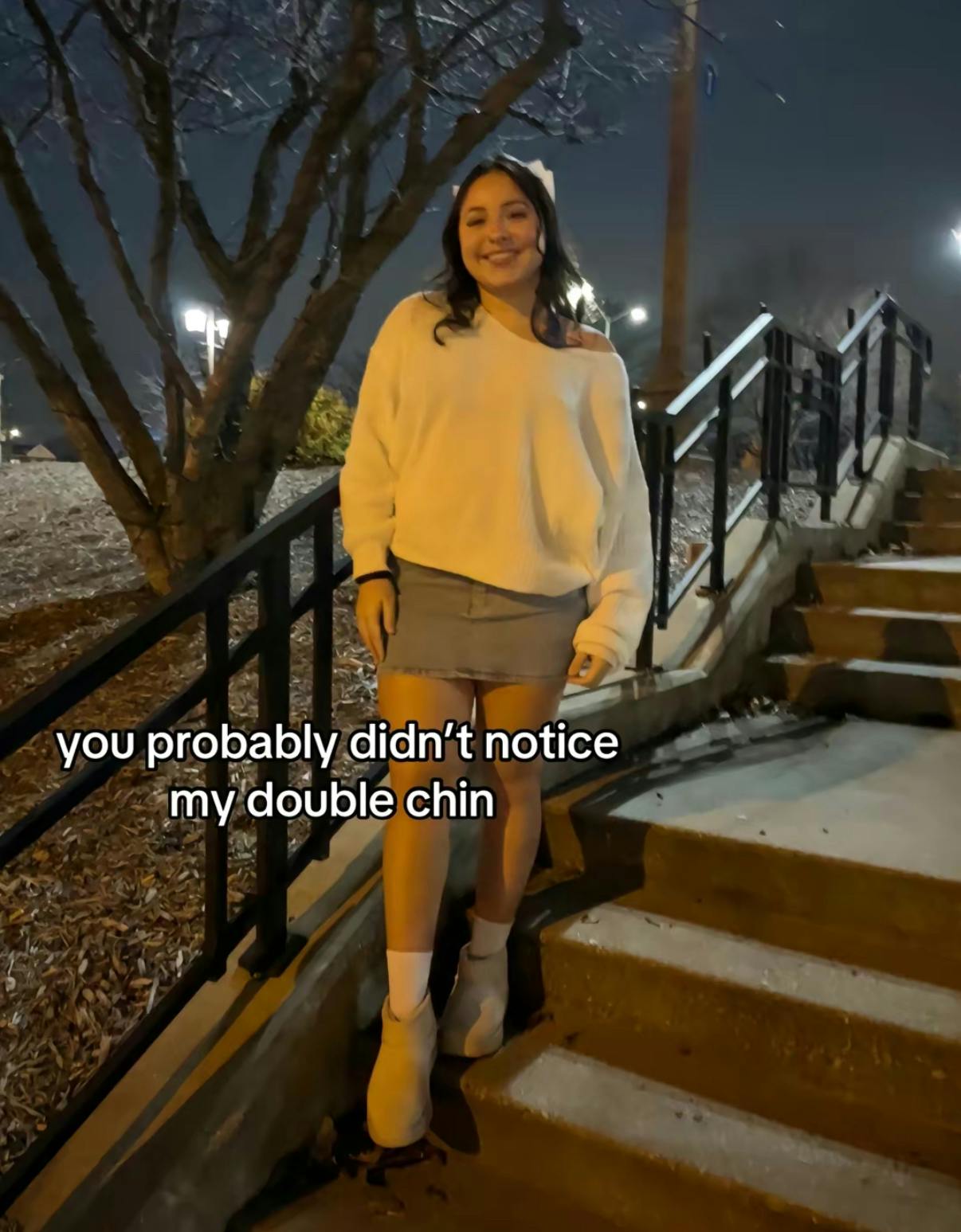 TikTok photo of a young woman smiling for the camera standing on a staircase outside at night. Text overlay reads, 'you probably didn't notice my double chin'