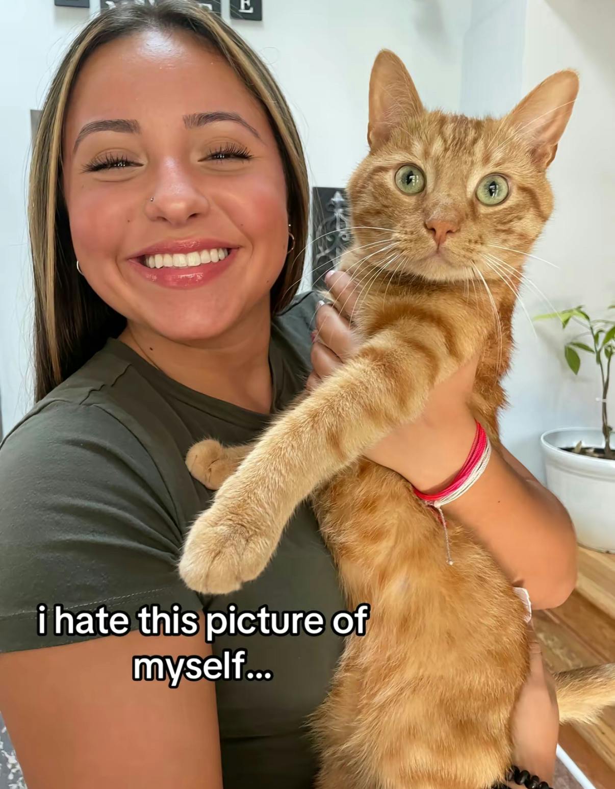 TikTok photo of a young woman smiling for the camera holding an orange cat. Text overlay reads, 'I hate this picture of myself...'