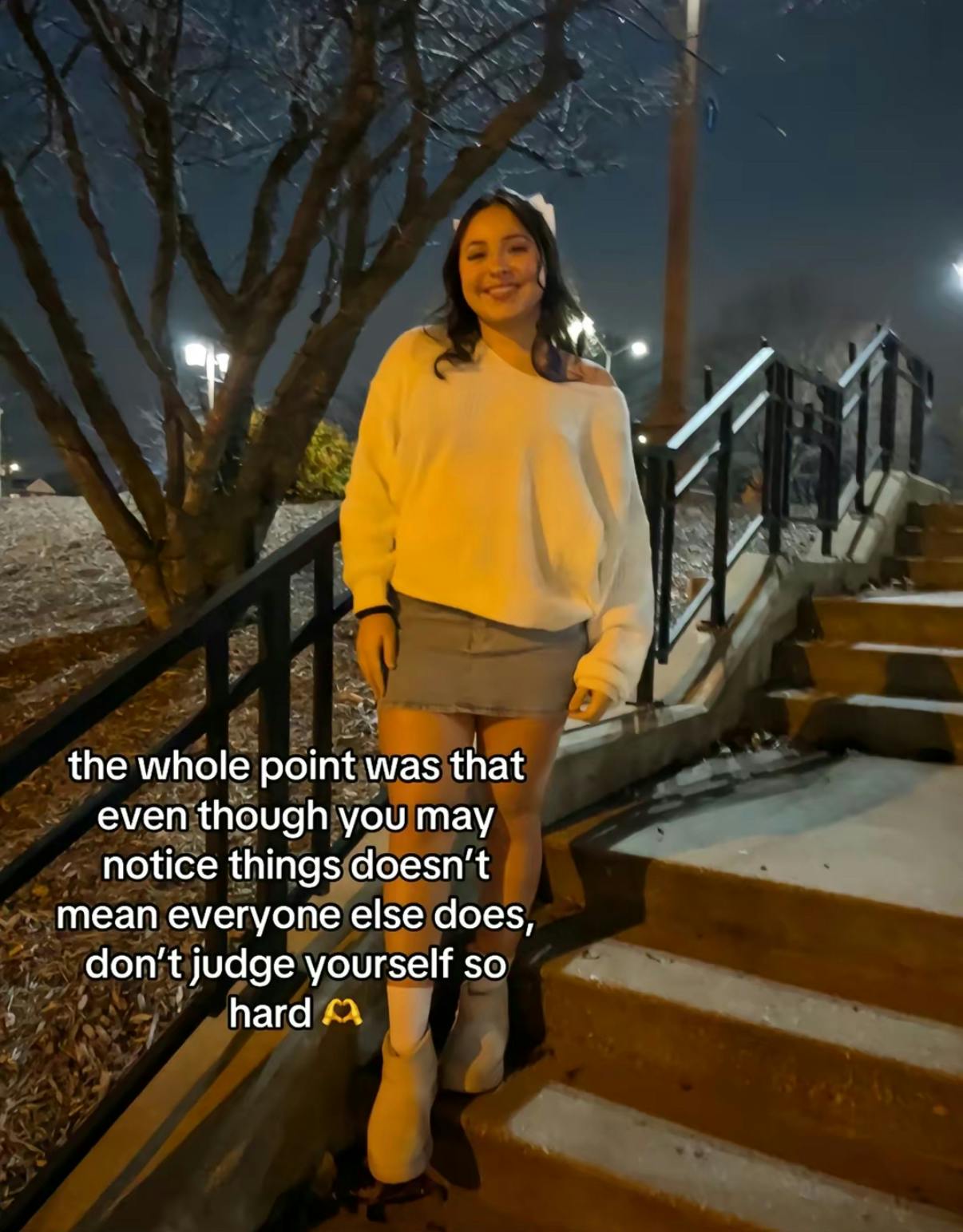 TikTok photo of a young woman smiling for the camera standing on a staircase outside at night. Text overlay reads, 'the whole point was that even though you may notice things doesn’t mean everyone else does, don’t judge yourself so hard.'