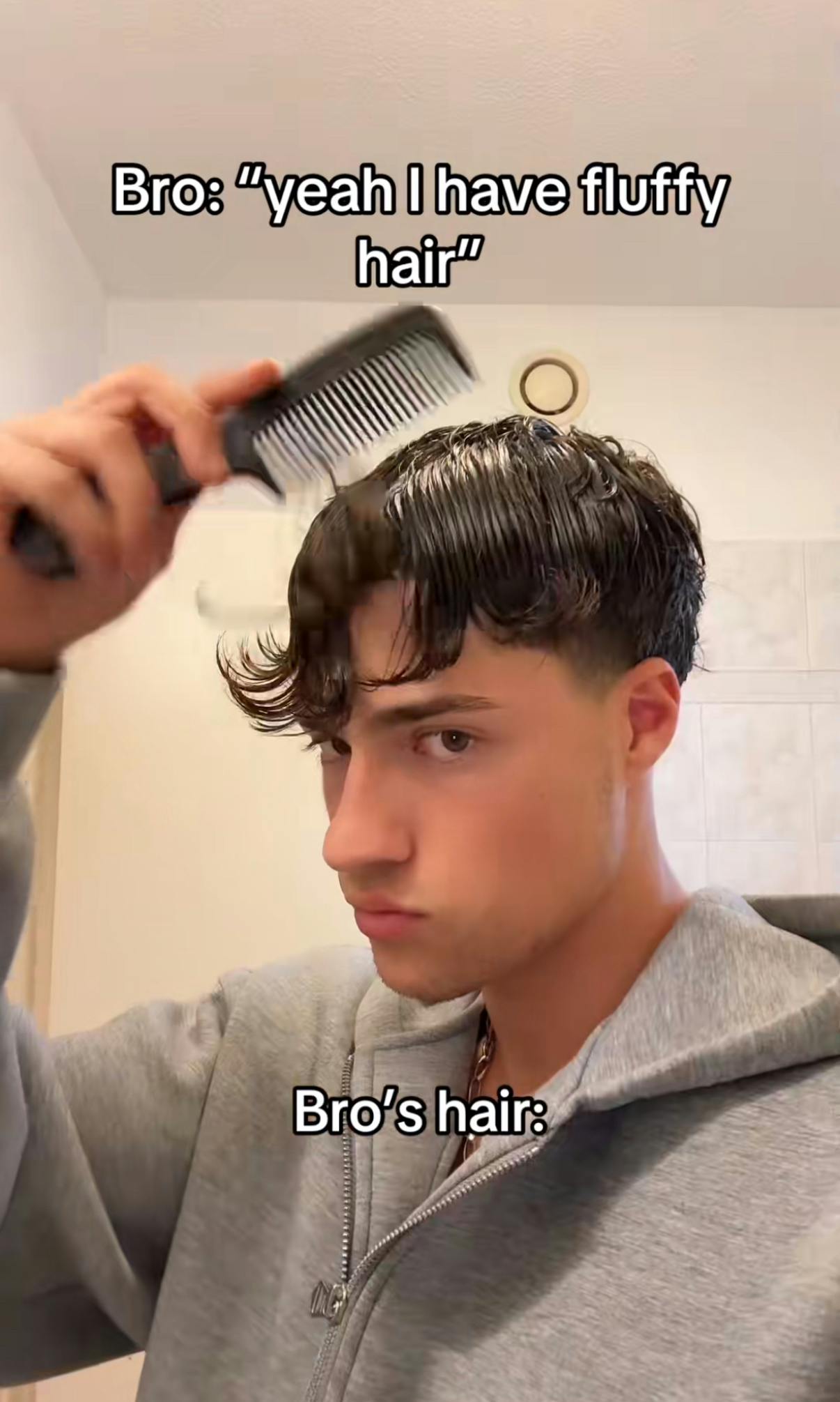 Screenshot of a young man with wet hair in cowlicks staring at the camera as he brushes it out with a comb. Text overlay reads, 'Bro: 'yeah I have fluffy hair' Bro's hair:'