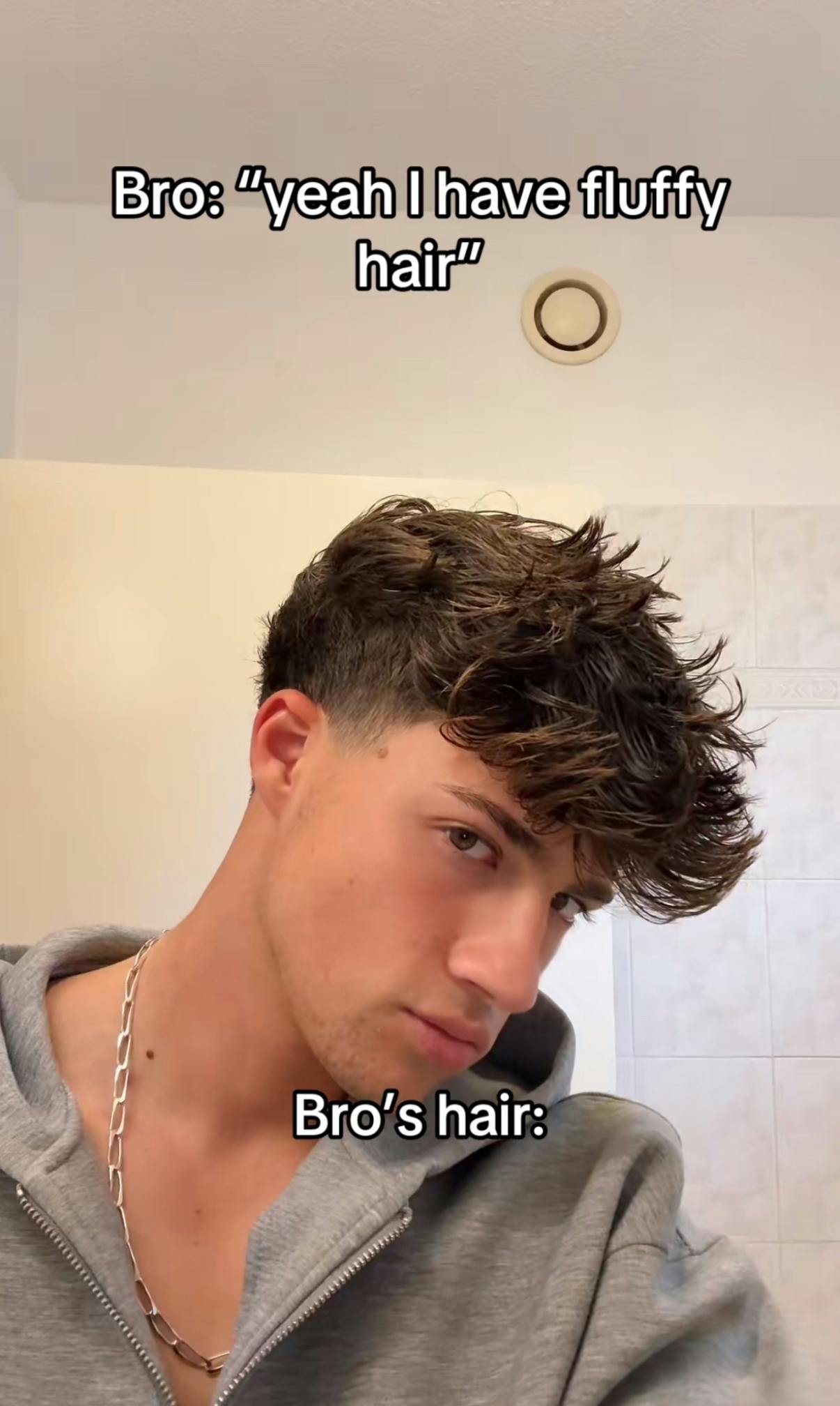 Screenshot of a young man with 'fluffy' hair staring at the camera. Text overlay reads, 'Bro: 'yeah I have fluffy hair' Bro's hair:'