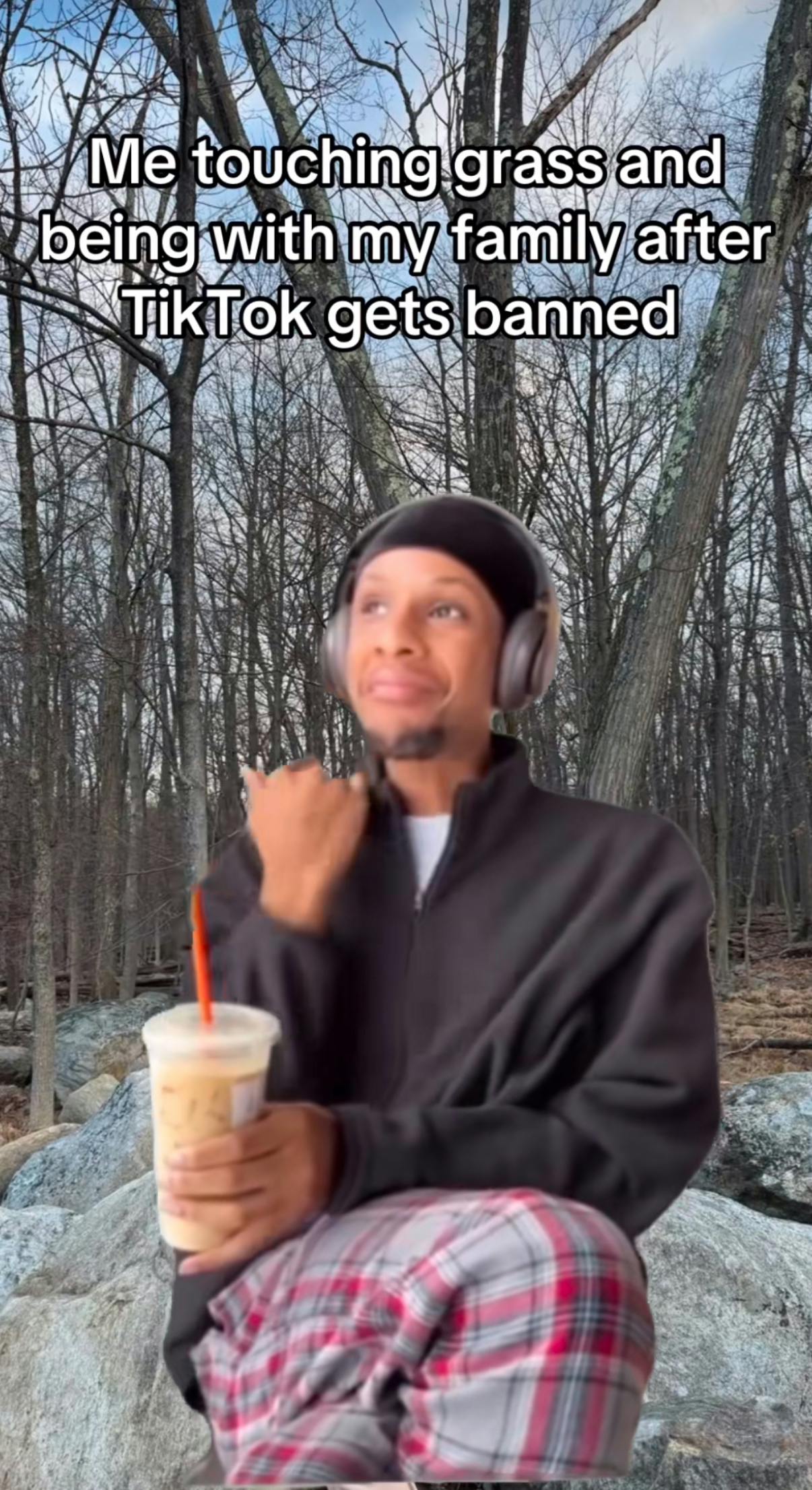 TikTok screenshot of a cold-looking nature scene and a man green screened over top in cozy pyjama bottoms, sweater, an iced coffee, and headphones. Text overlay reads, 'Me touching grass and being with my family after TikTok gets banned.'