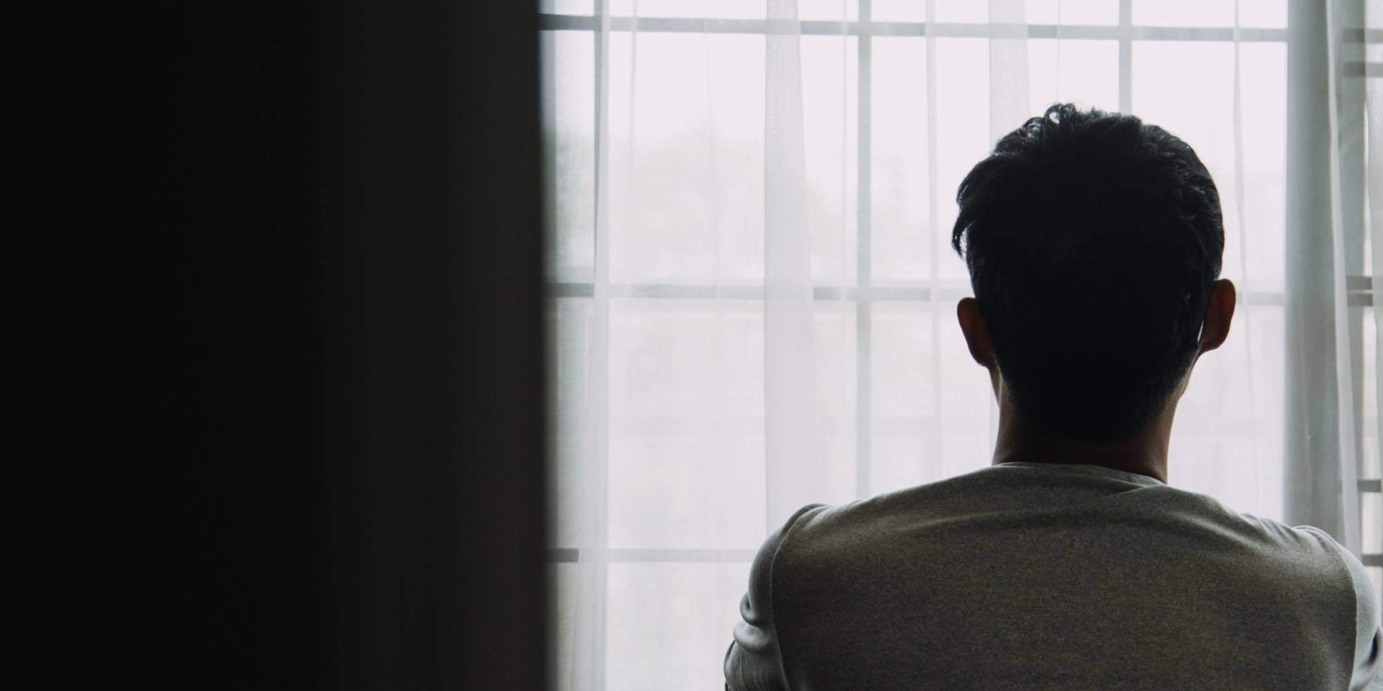 A person sitting in a dark room looking out the window.