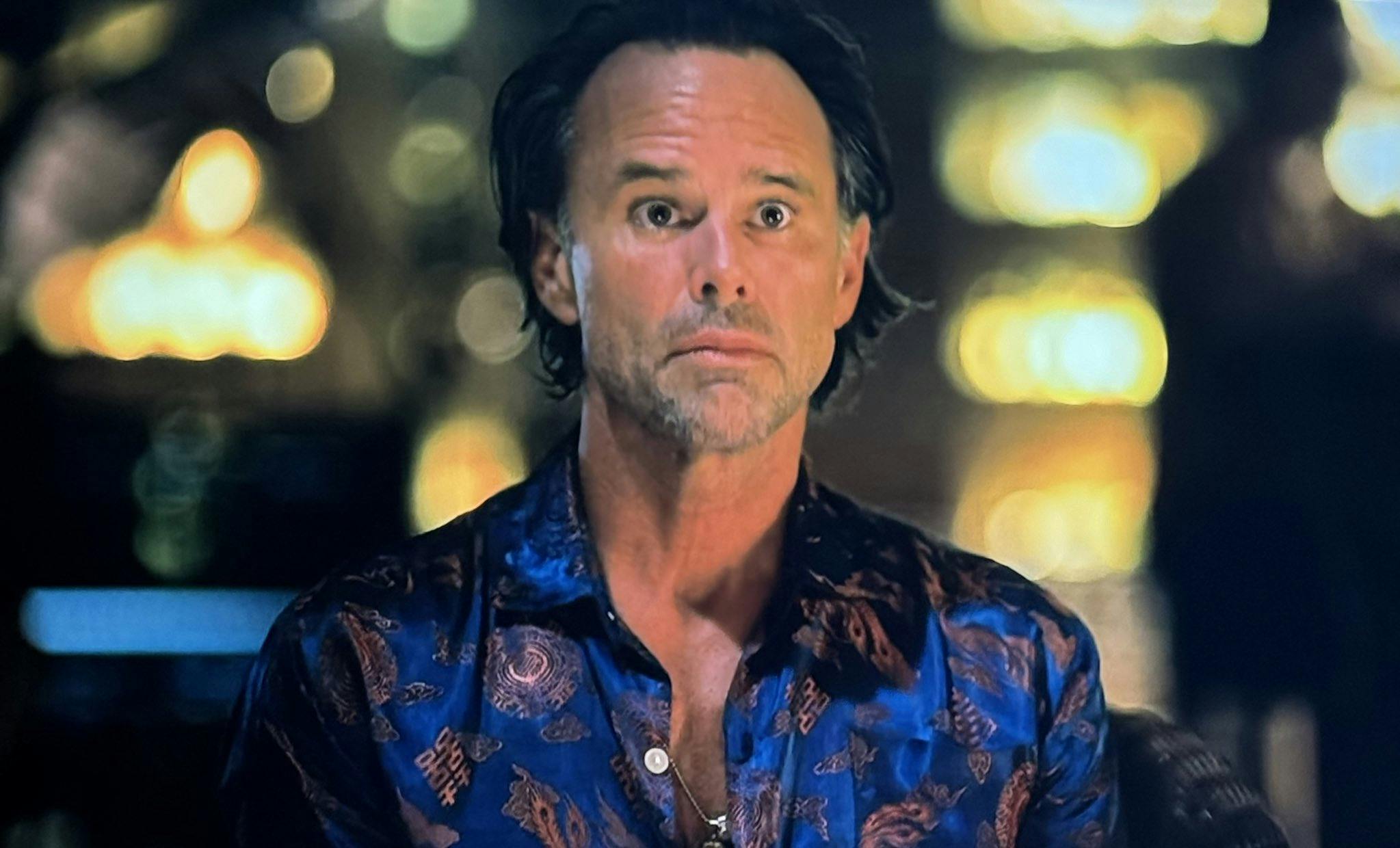 Rick Hatchett from The White Lotus staring with wide eyes in a blue and gold shirt.