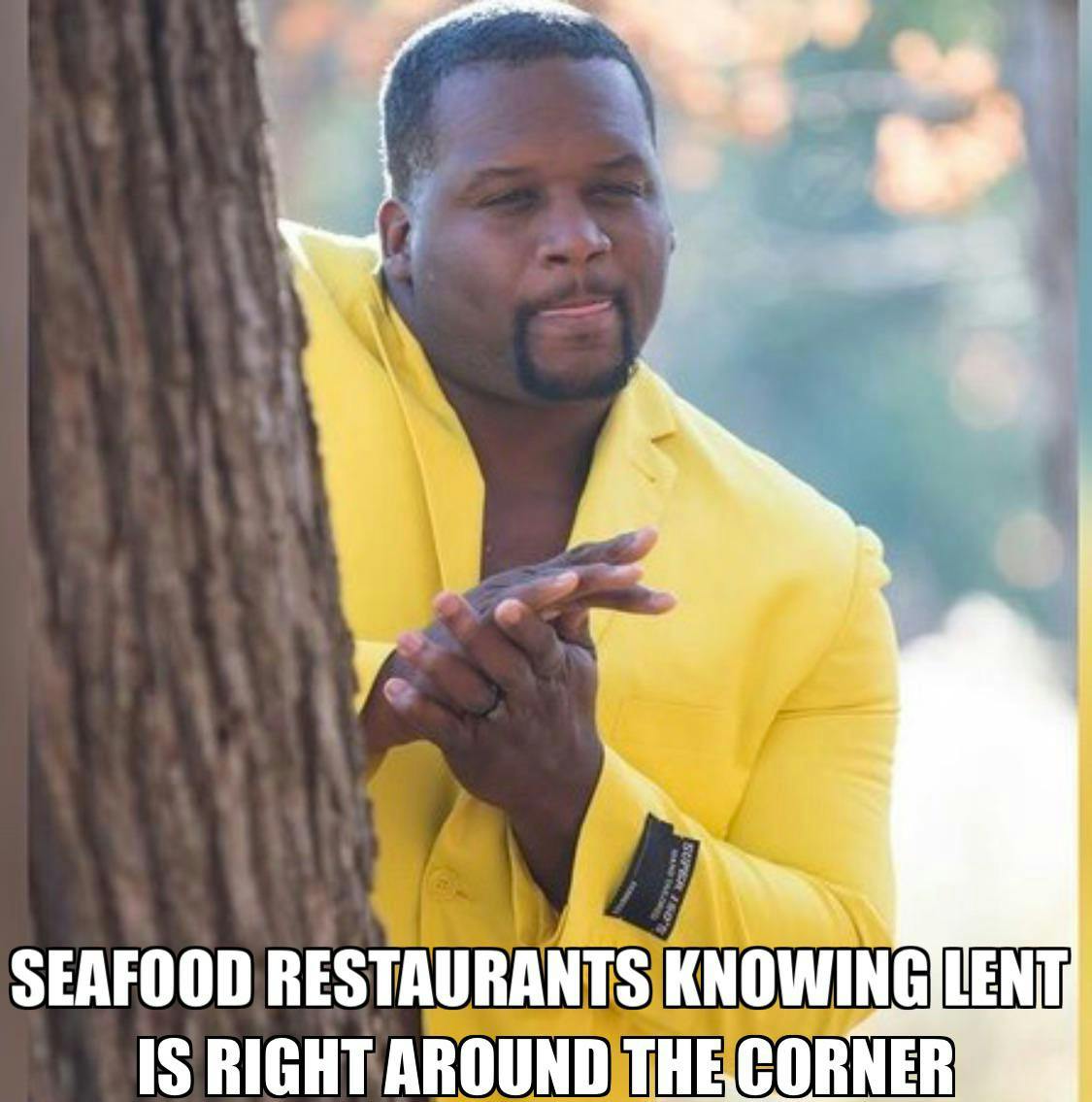 Lent meme, text reads, 'Seafood restaurants knowing Lent is right around the corner.' with a man in a yellow suit rubbing his hands together behind a tree.