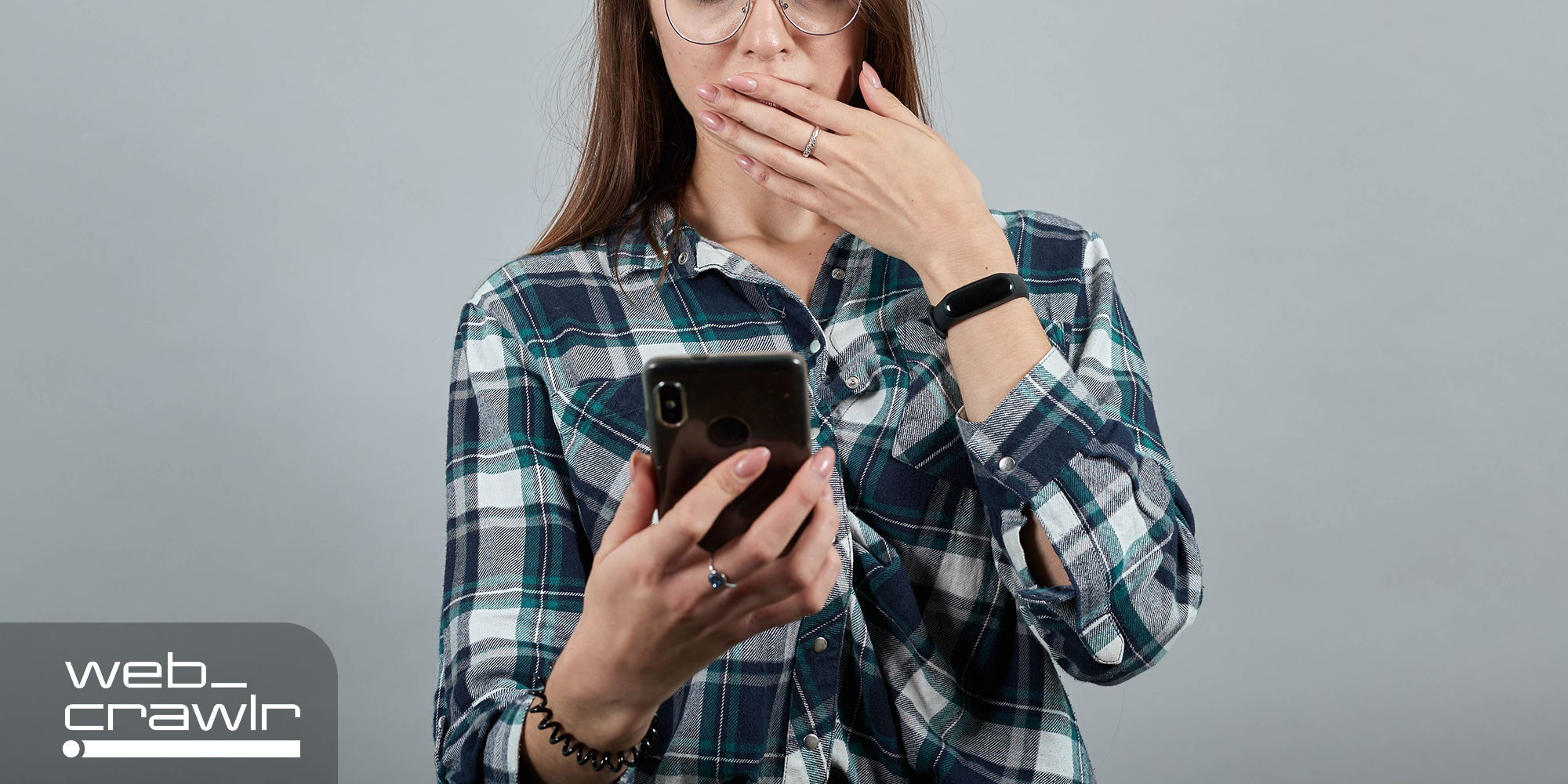 A person looking at an iPhone with her hand over her mouth. The Daily Dot newsletter web_crawlr logo is in the top left corner.
