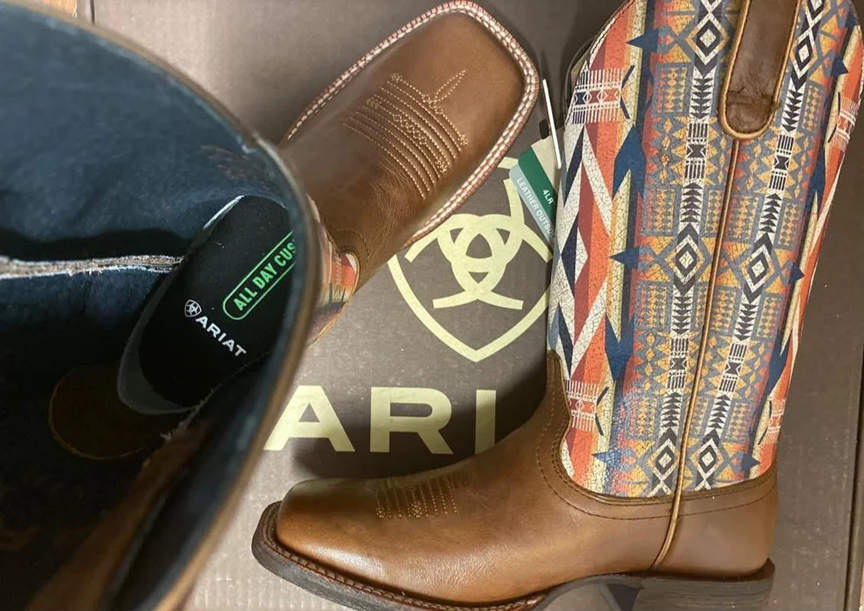 A photo of a pair of brown leather Ariat boots with patterned sides showing the length of one and the interior of the other, in good condition.