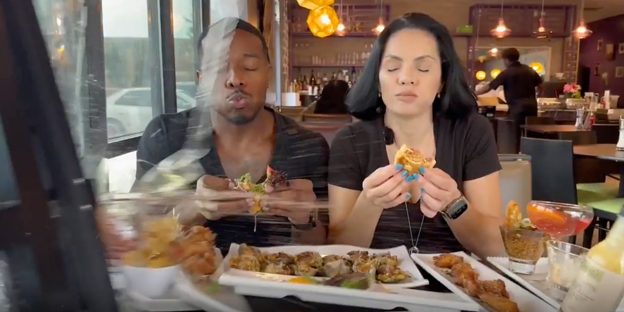 Influencers Nina Santiago and Patrick Blackwood eating burgers in a restaurant just as glass begins to shatter as a car plows into the restaurant.