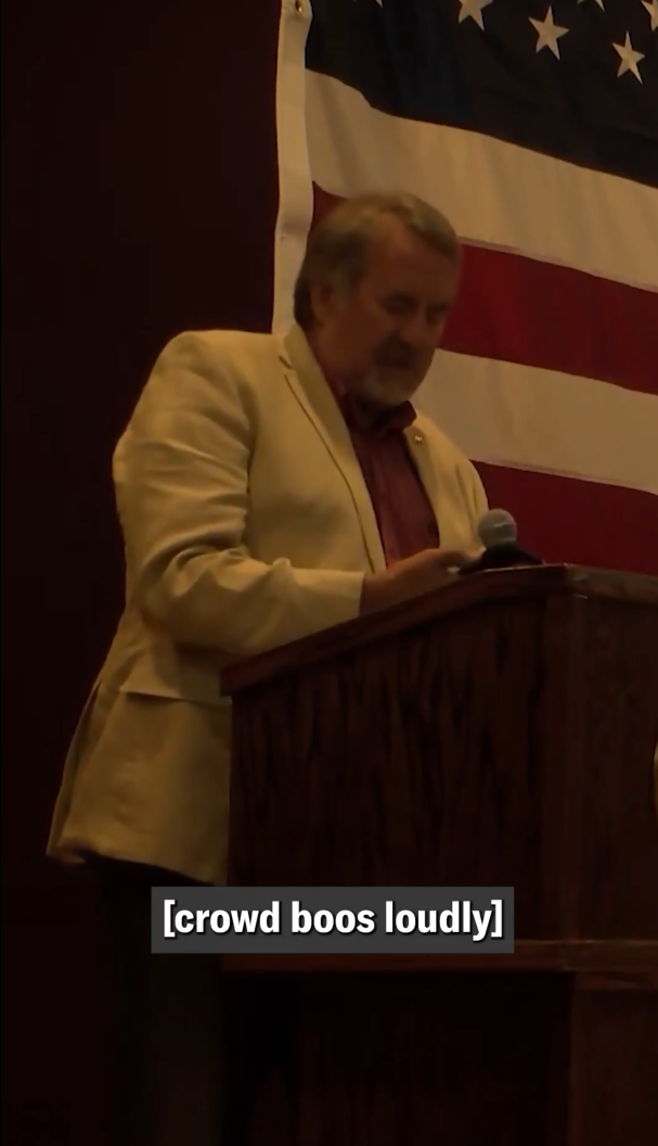 Rep. Doug LaMalfa standing at a podium and looking down at his phone with a caption reading '[crowd boos loudly].'