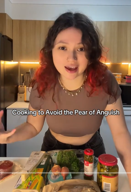 TikTok video with a woman speaking to the camera over ingredients with a caption reading 'Cooking to Avoid the Pear of Anguish.'
