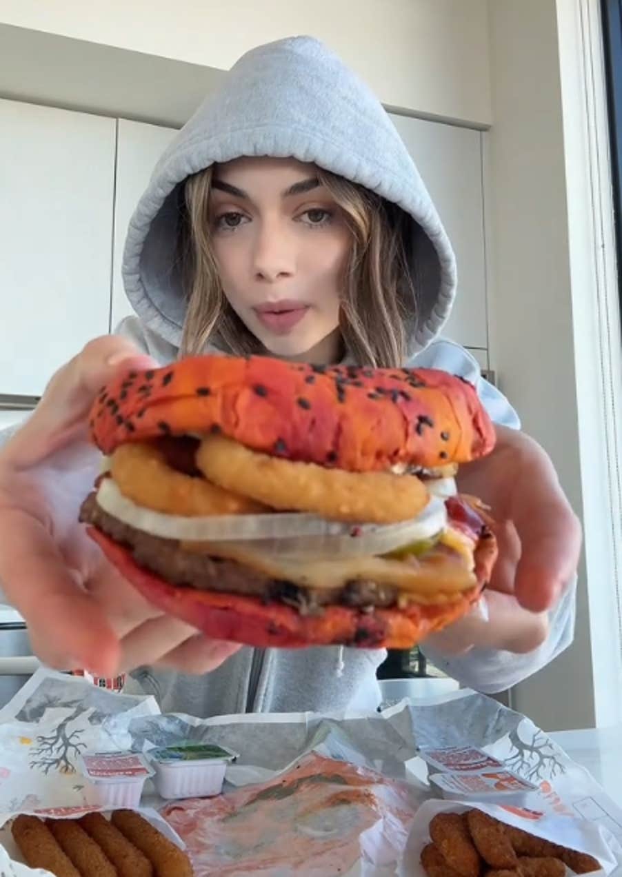 TikTok video of a woman in a hoodie holding up a Halloween Whopper for the camera.