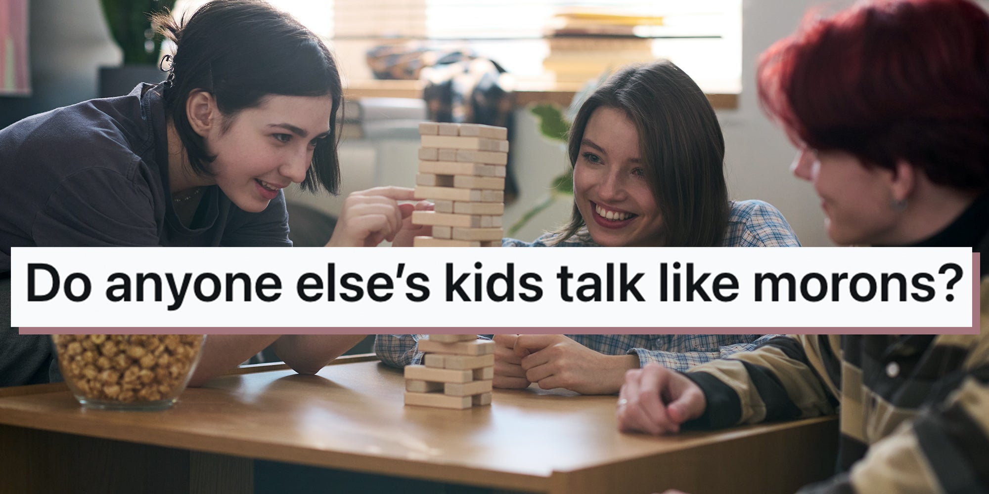 Smiling teenage girl playing board game with two friends at home or in school dorm and removing wooden block from tower. Text overlay from Reddit reads, 'Do anyone else’s kids talk like morons?'
