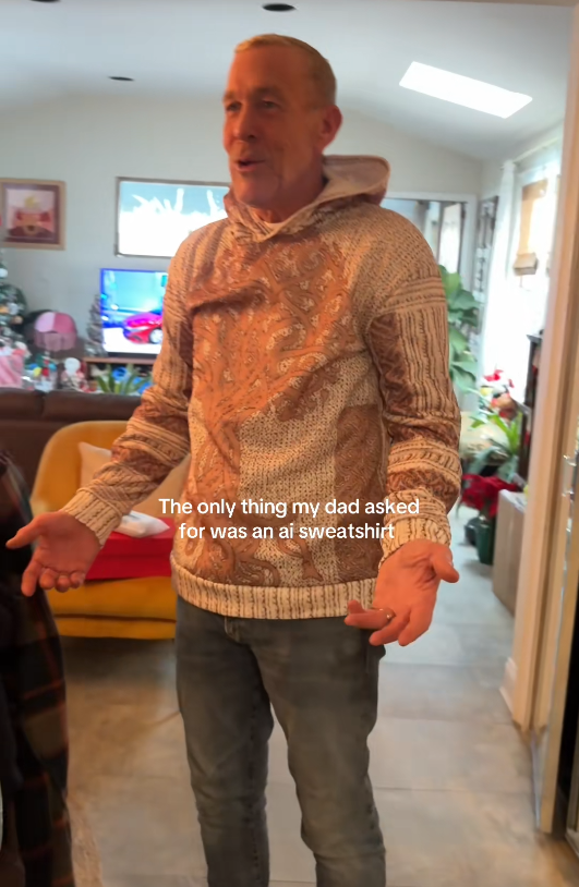 TikTok video with a man spreading his arms in a tan tree sweater with a caption reading, 'The only thing my dad asked for was an ai sweatshirt.'