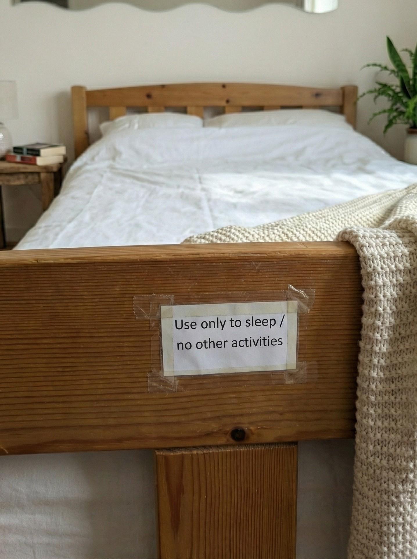 Photo of a bed taken from the foot with a sign taped on the bed frame reading 'Use only to sleep / no other activities.'
