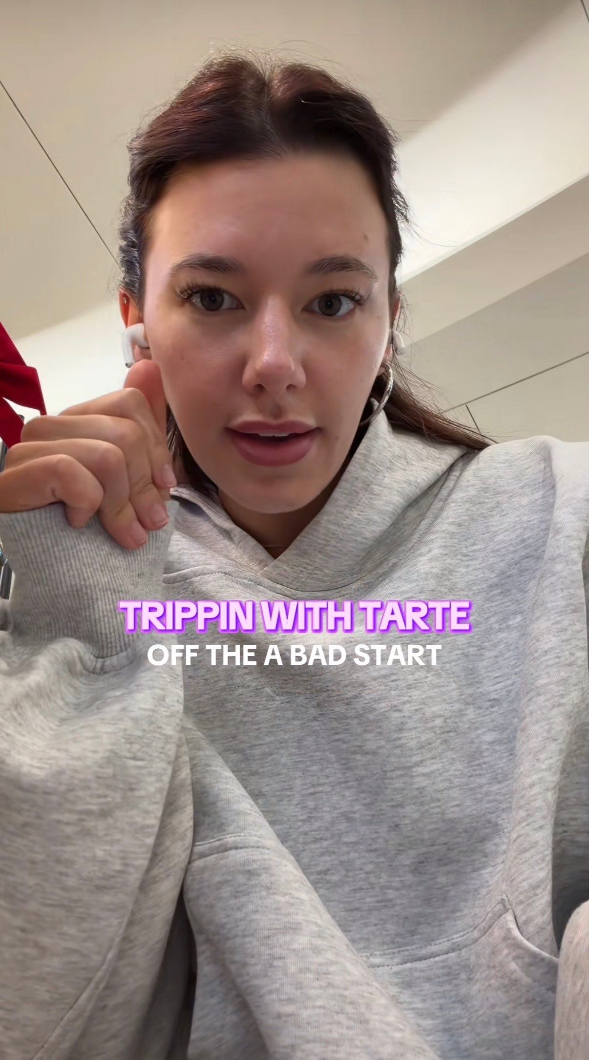 A woman with red hair and a grey hoodie talking at her camera, leaning down slightly. Text overlay reads, "Trippin with Tarte off the [sic] a bad start."