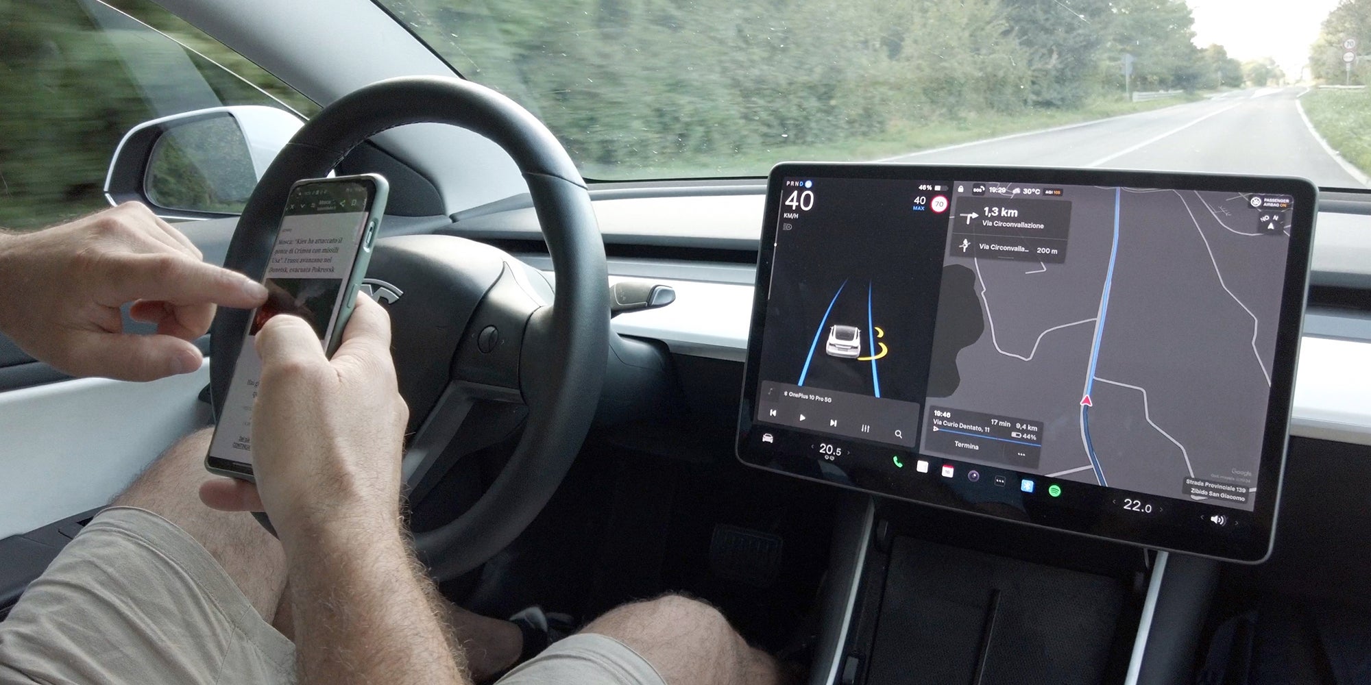 Autopilot and Self-Driving Features in Tesla Electric car; Man sitting behind the wheel of a Tesla car while on his phone.