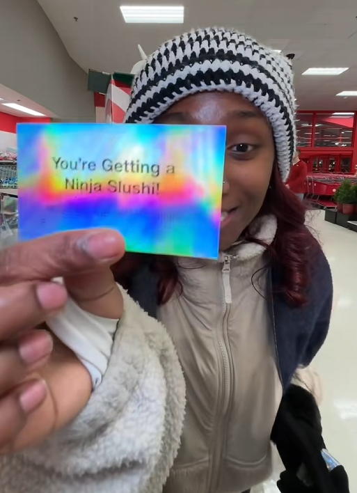 TikTok video of a woman in Target showing a card to the camera that says 'You're Getting a Ninja Slushi!'