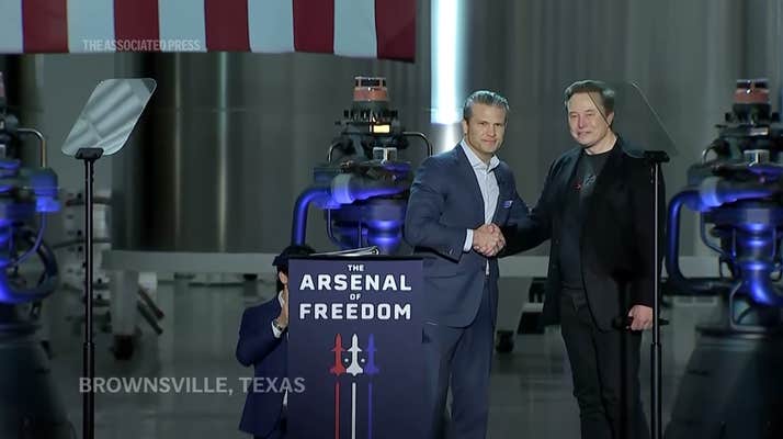Pete Hegseth and Elon Musk on a stage shaking hands and staring out at an audience.