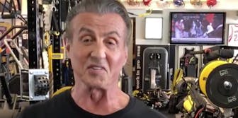 Sylvester Stallone smiles in front of some weight lifting equipment